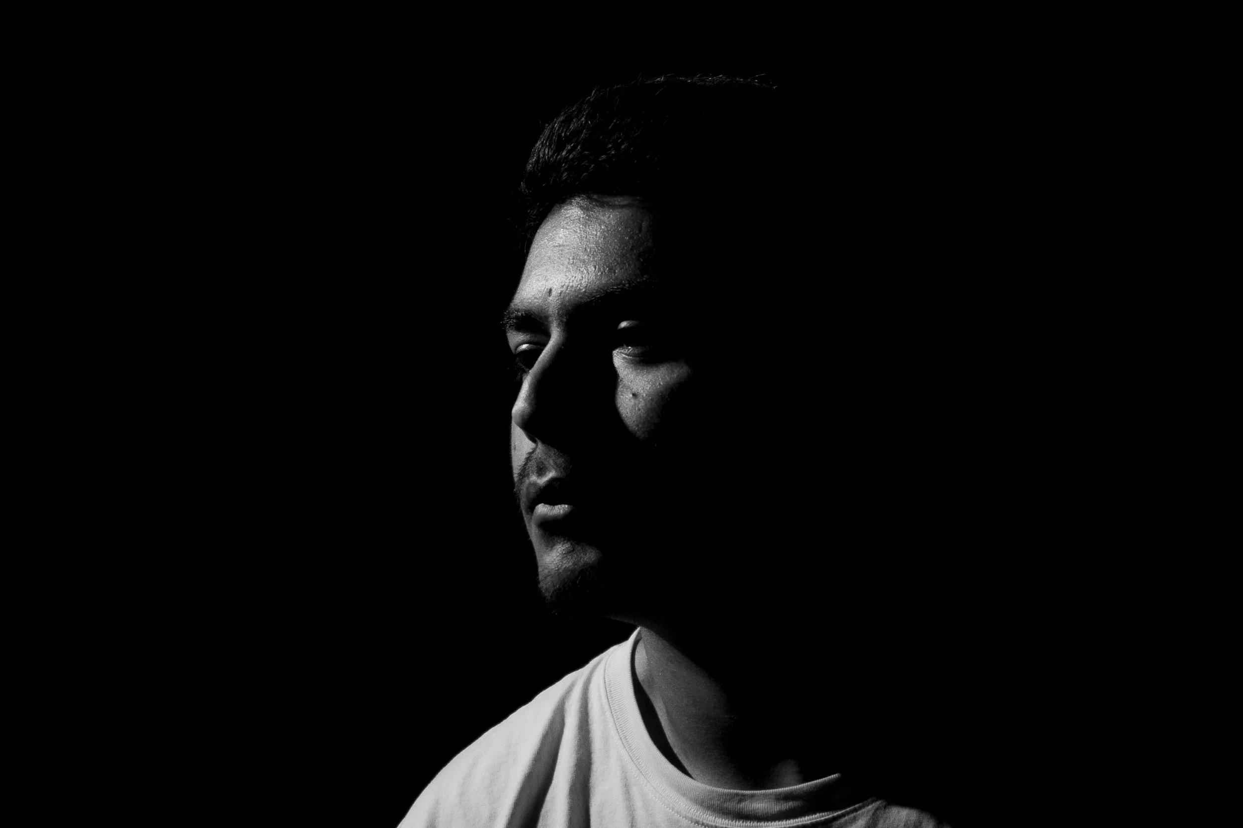Black and white portrait of a young man with partial shadow across his face, facing slightly to the right, wearing a light-colored shirt.