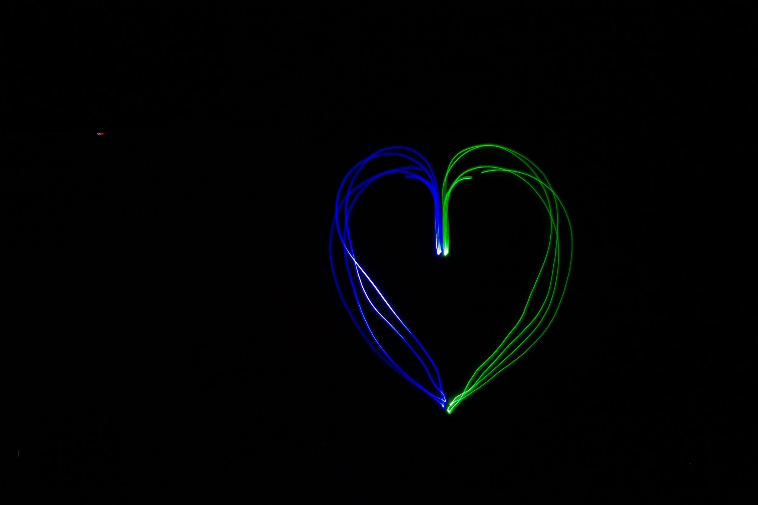 Light painting of a heart shape created with blue and green light trails against a black background.
