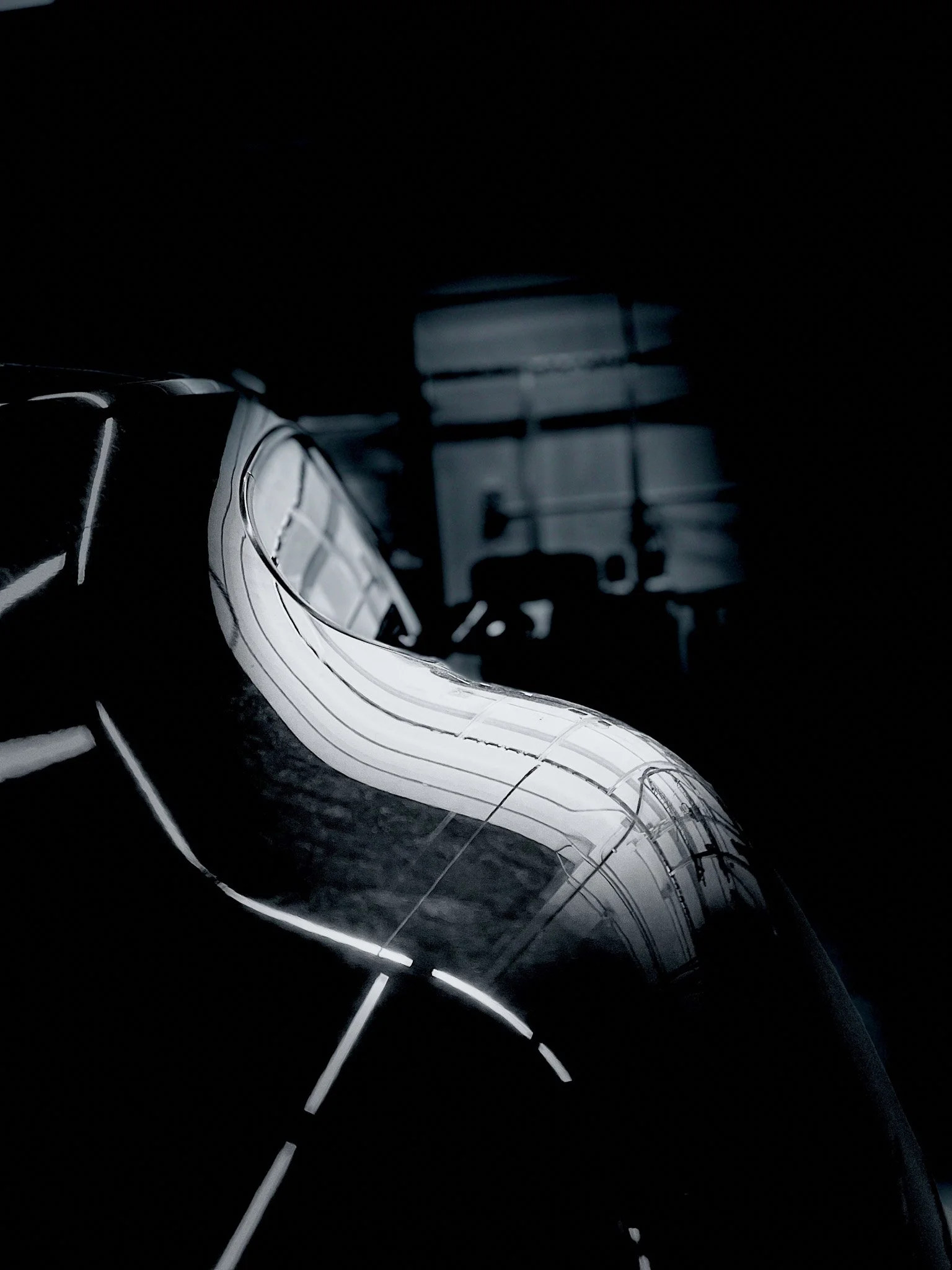 Close-up of a sleek, reflective, futuristic sculpture with glowing lines in a dark room.