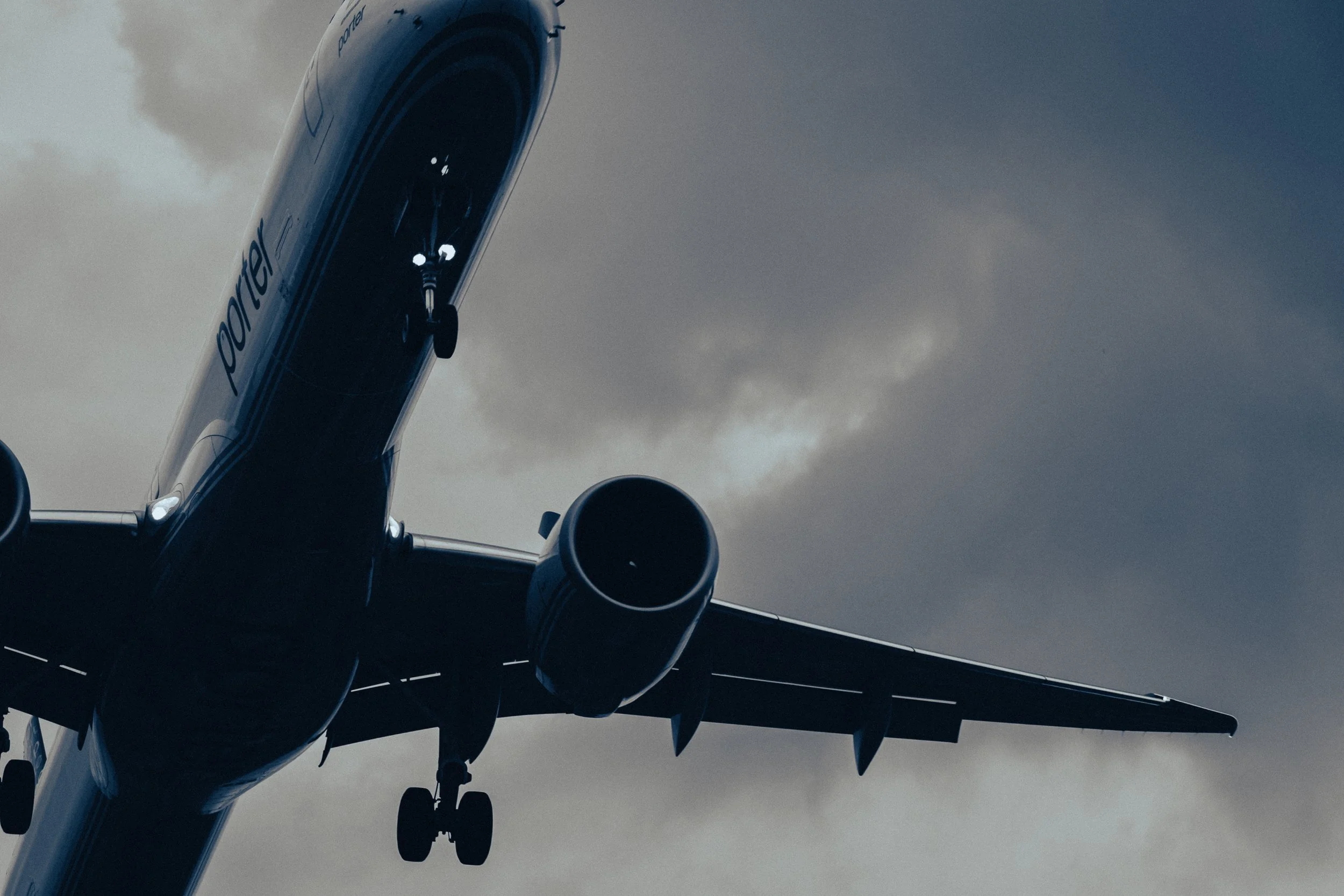A commercial airplane flying through the cloudy sky with landing gear extended.