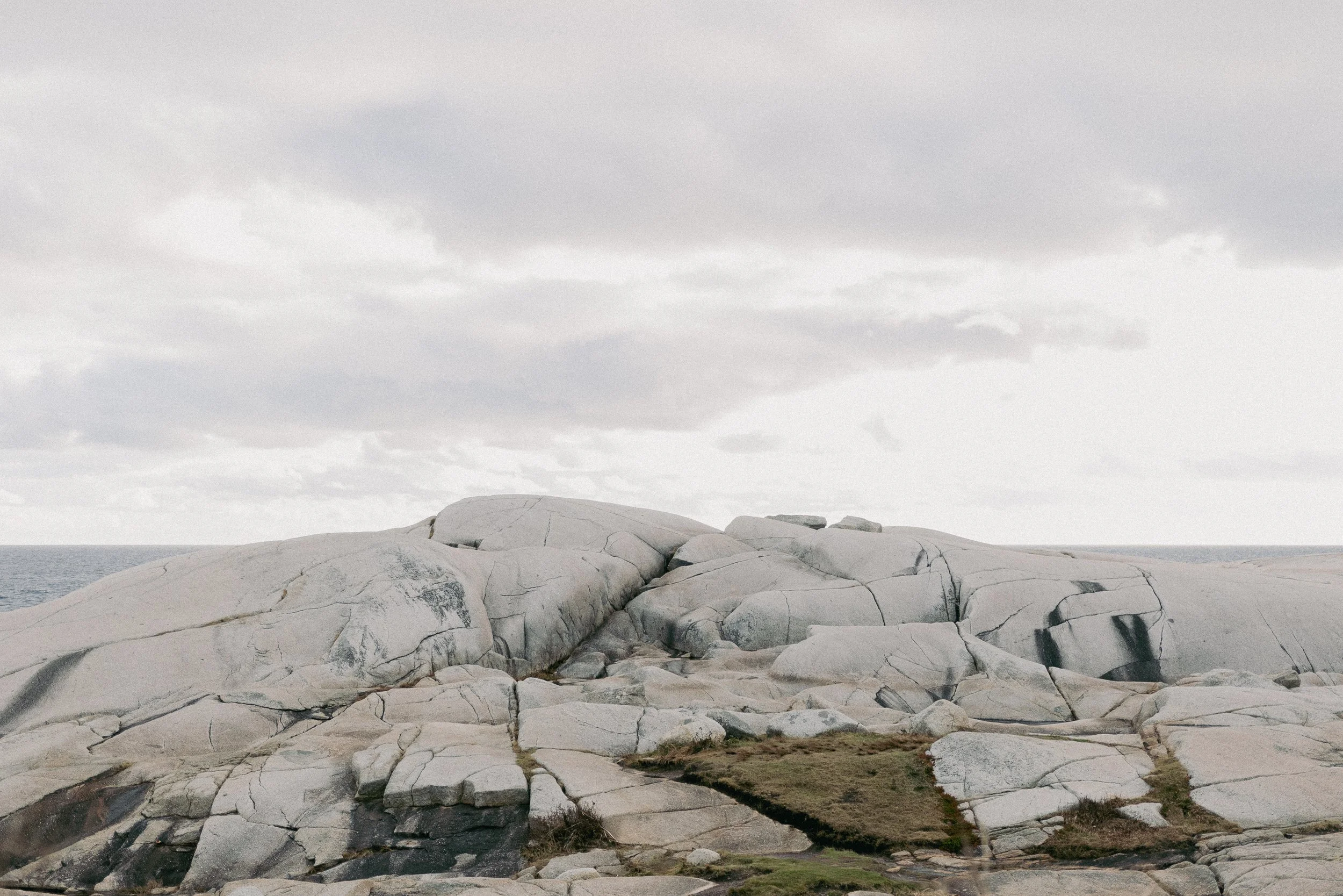 Large white granite rocks near a cloudy sky and the ocean in the background.