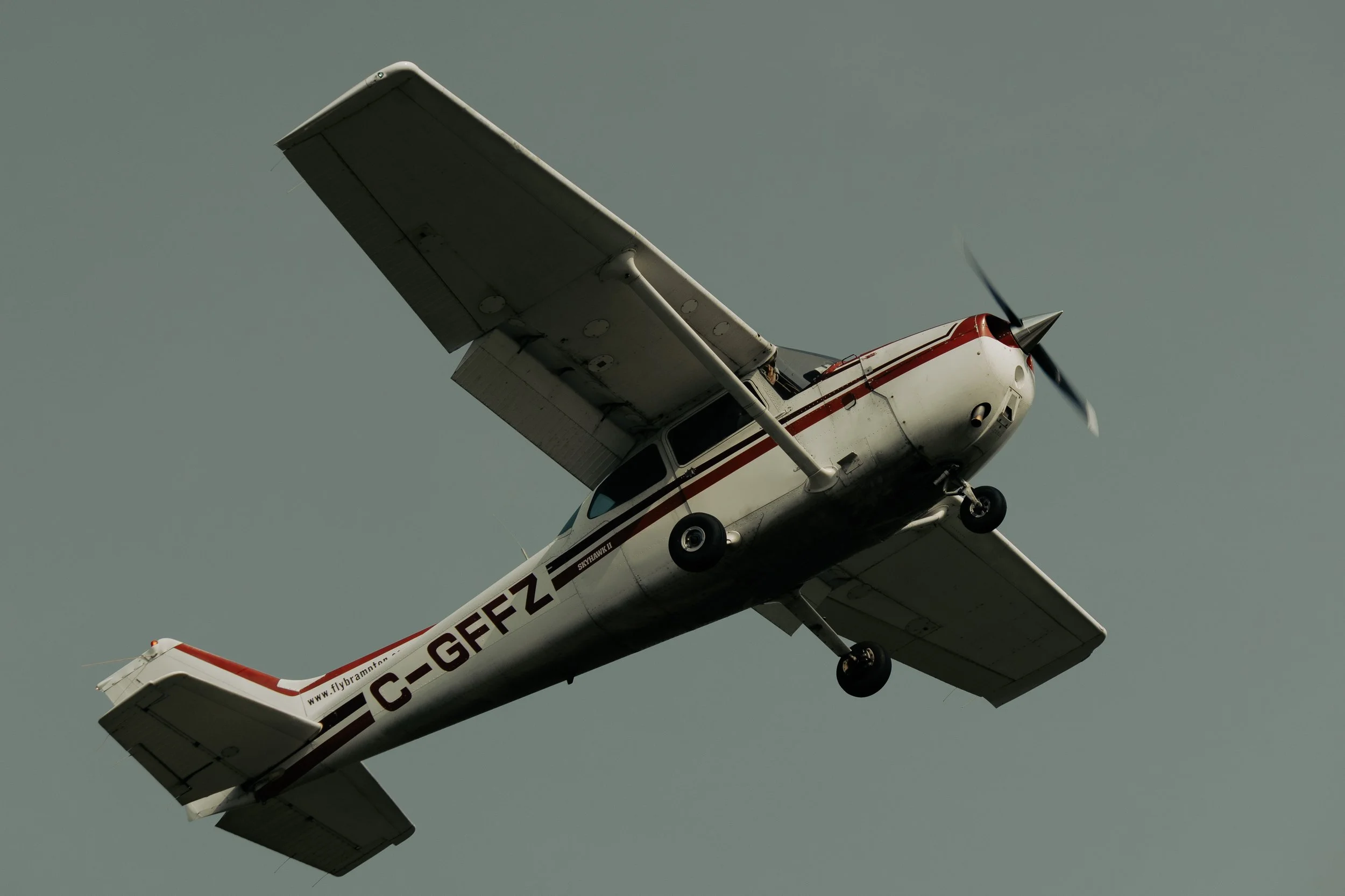 A small airplane with white and red colors, flying against a cloudy sky, viewed from below.