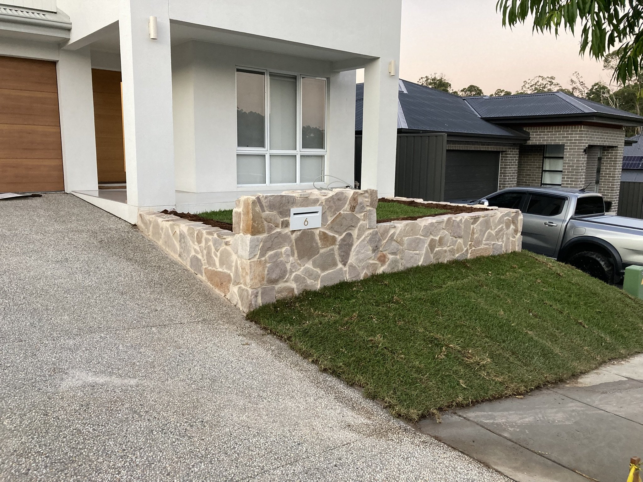 Modern house with a stone-bordered front yard, green lawn, large window, and a parked truck in the driveway.