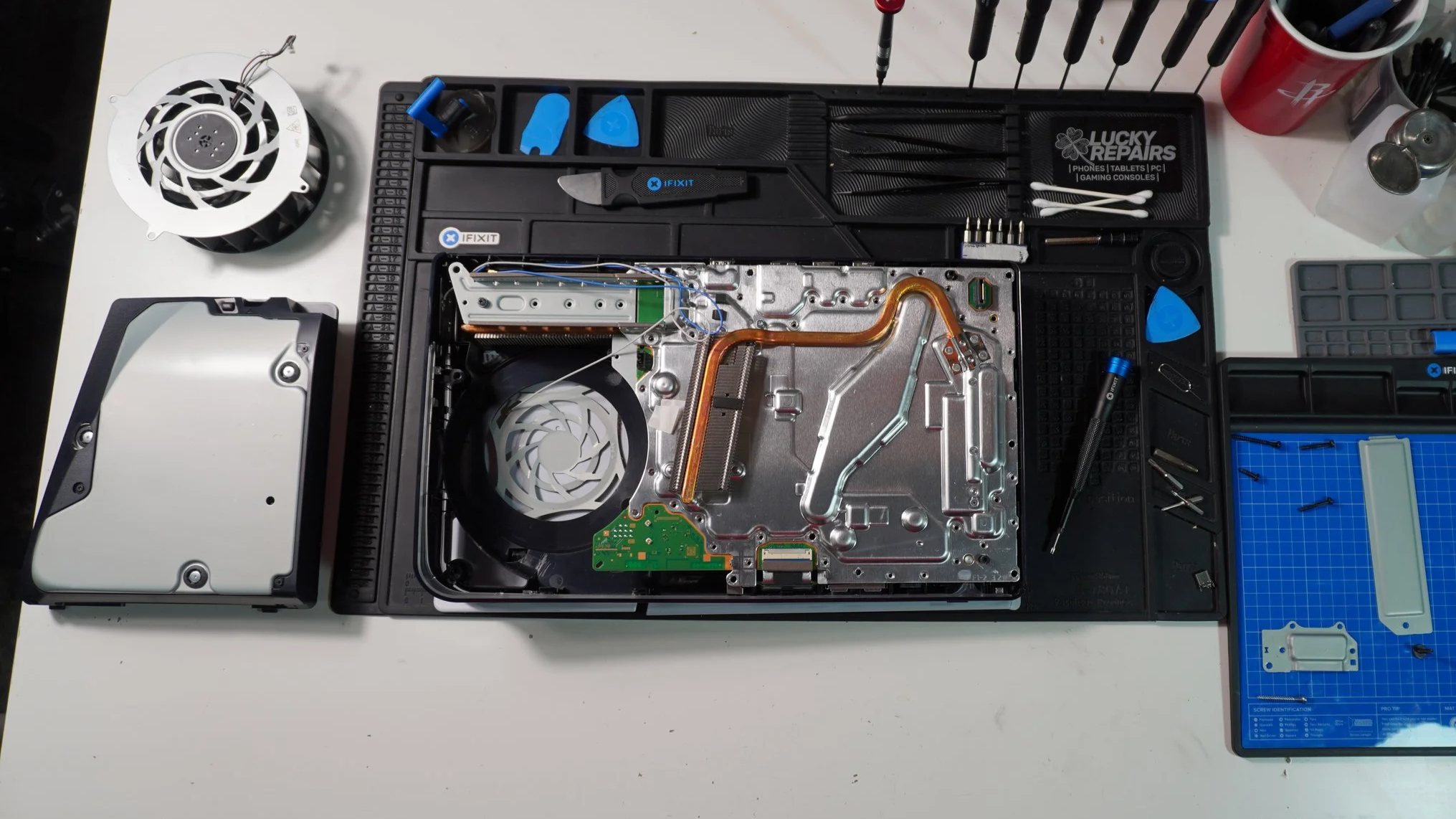 Top view of a disassembled gaming console with internal components exposed on a workbench, surrounded by tools and accessories.