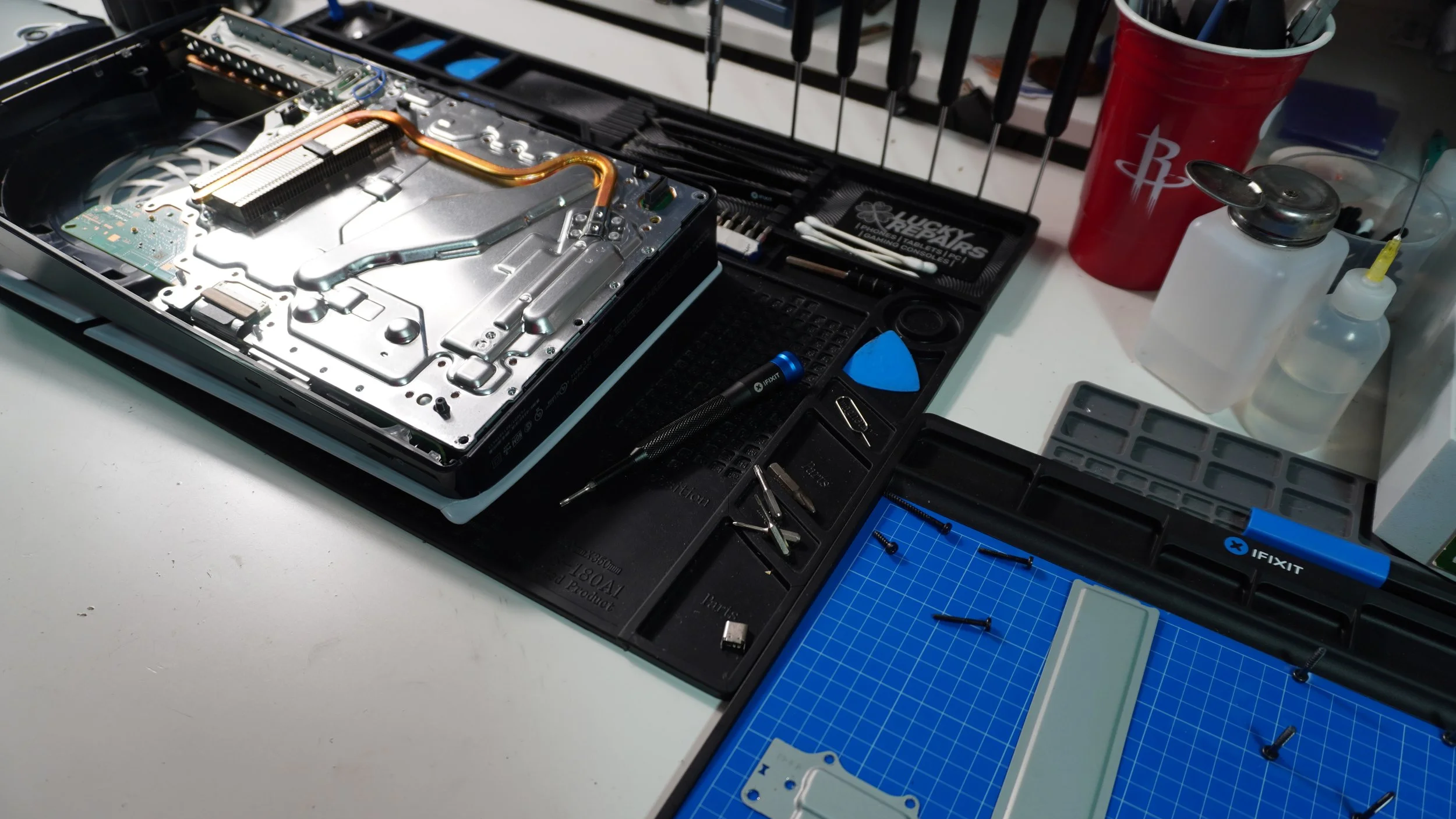 Open electronic device repair workstation with disassembled case, tools, small bottles, and electronic parts.