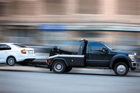 A black pickup truck towing a white sedan on a highway