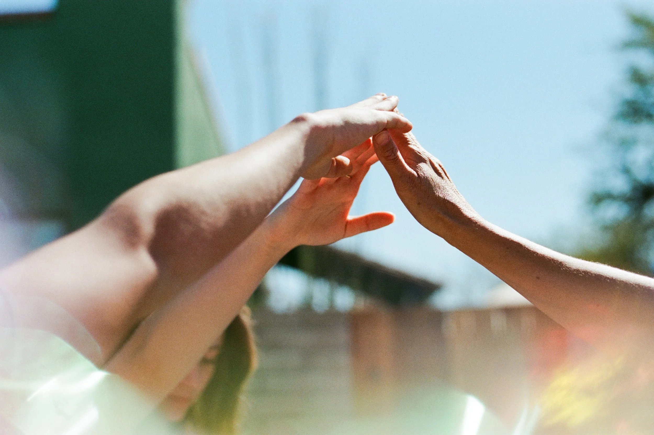 Two people reaching their hands out to each other outdoors on a sunny day.