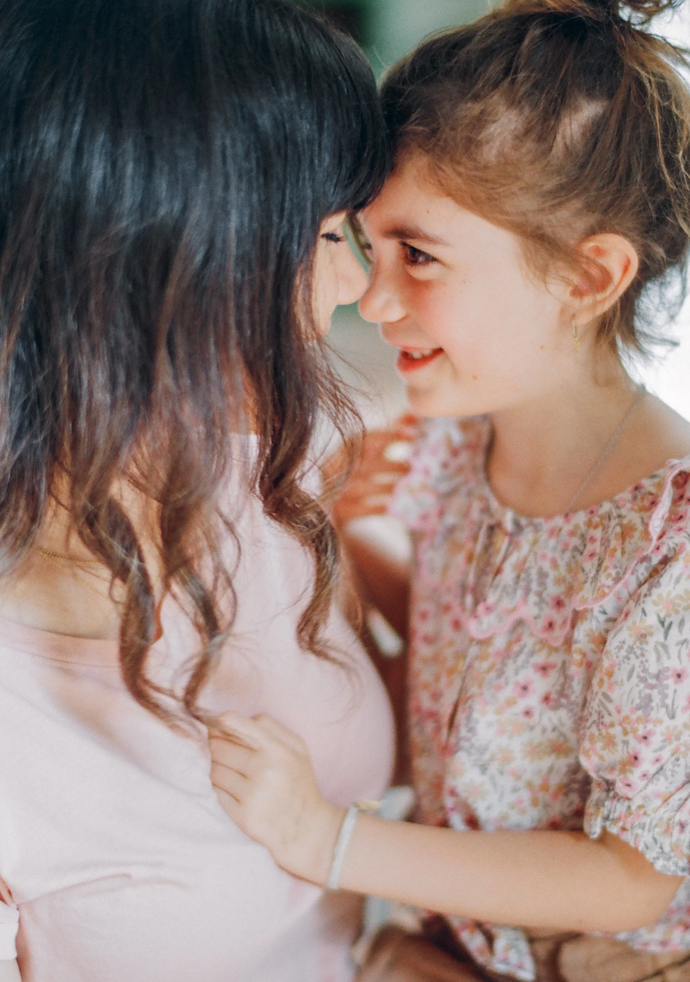 A woman and a young girl are touching foreheads and smiling at each other, showing affection and joy.