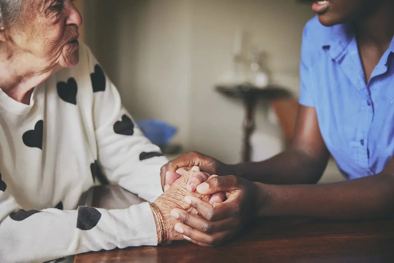 A young woman holding hands with an elderly woman, comforting and supporting her.