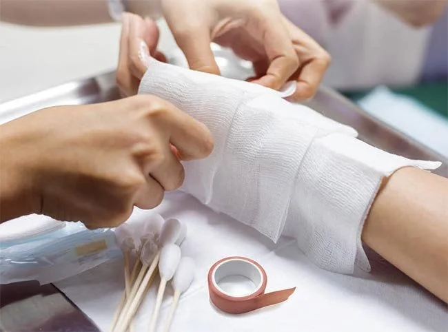 A healthcare professional wrapping a person's arm with a bandage in a medical setting.