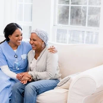 A nurse comforting a smiling patient in a hospital room with large windows.