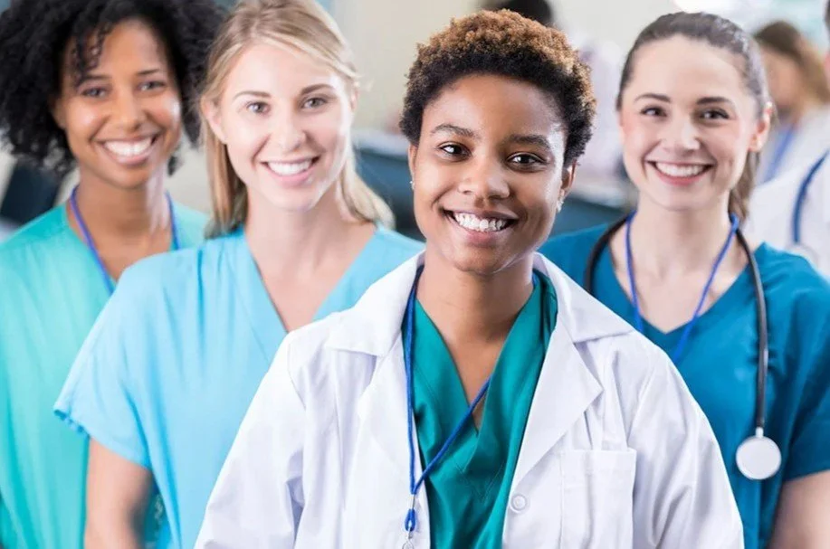 Group of smiling female healthcare professionals in scrubs and lab coat.