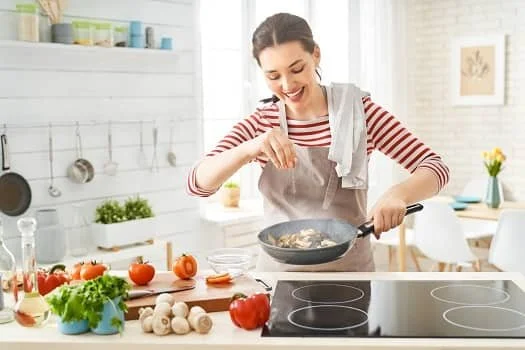 Woman cooking in a bright kitchen with vegetables on the counter.