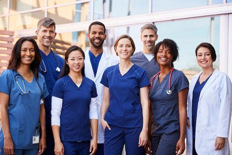 Group of healthcare professionals, including doctors and nurses, standing outside a medical facility.