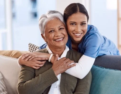 A young woman hugging an older woman, both smiling warmly in a home setting.