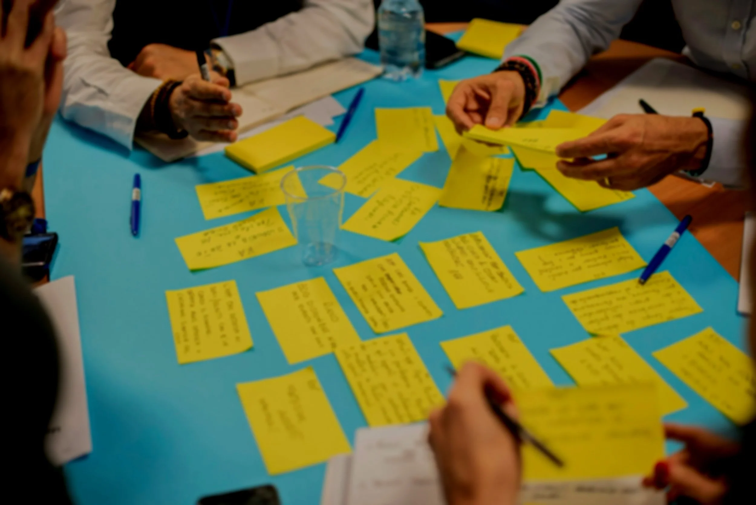 Menschen sitzen an einem Tisch und ordnen gelbe Post-it-Notizen mit handgeschriebenen Notizen darauf.