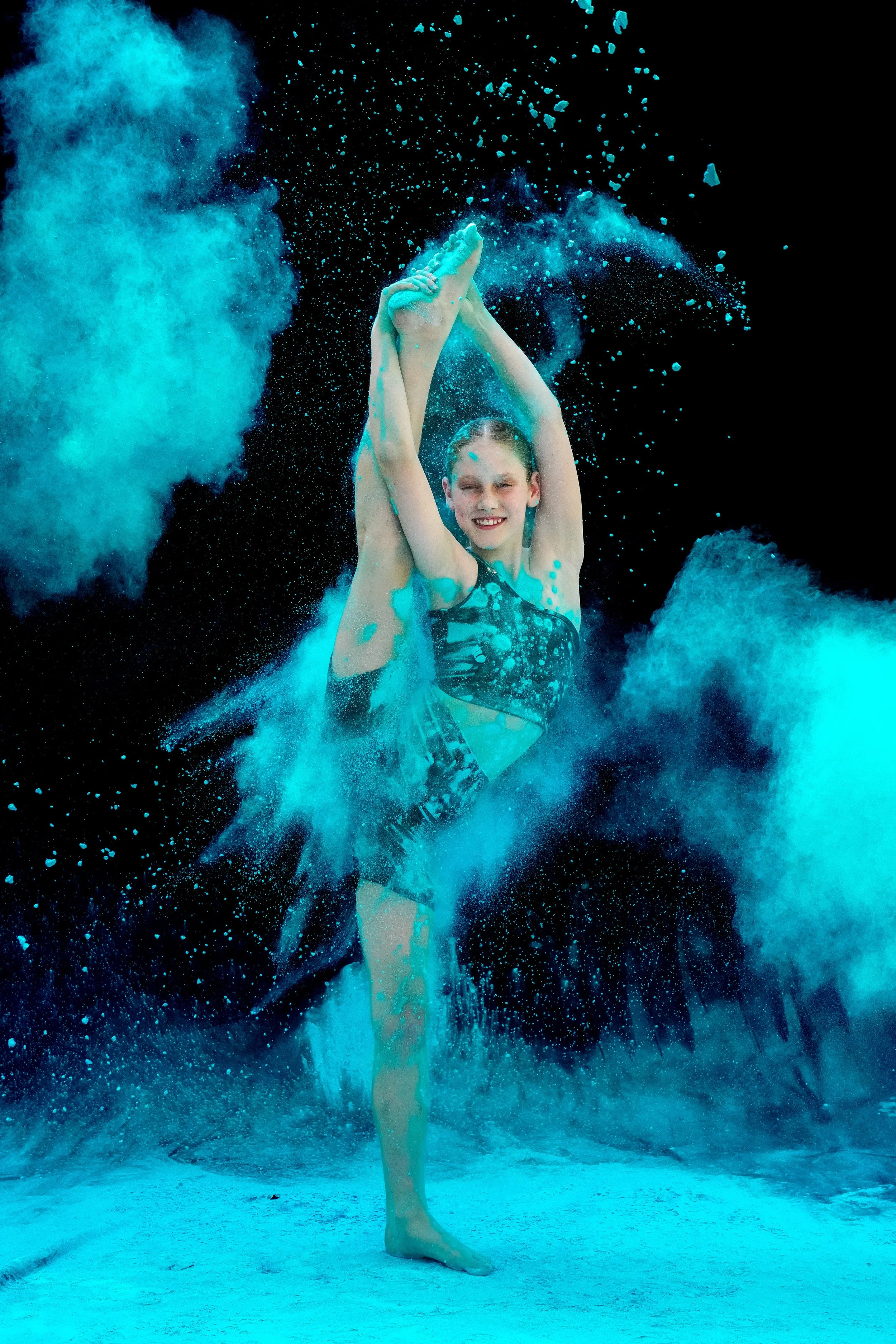 Dance Headquarters student performing a leg mount at photoshoot with blue powder.