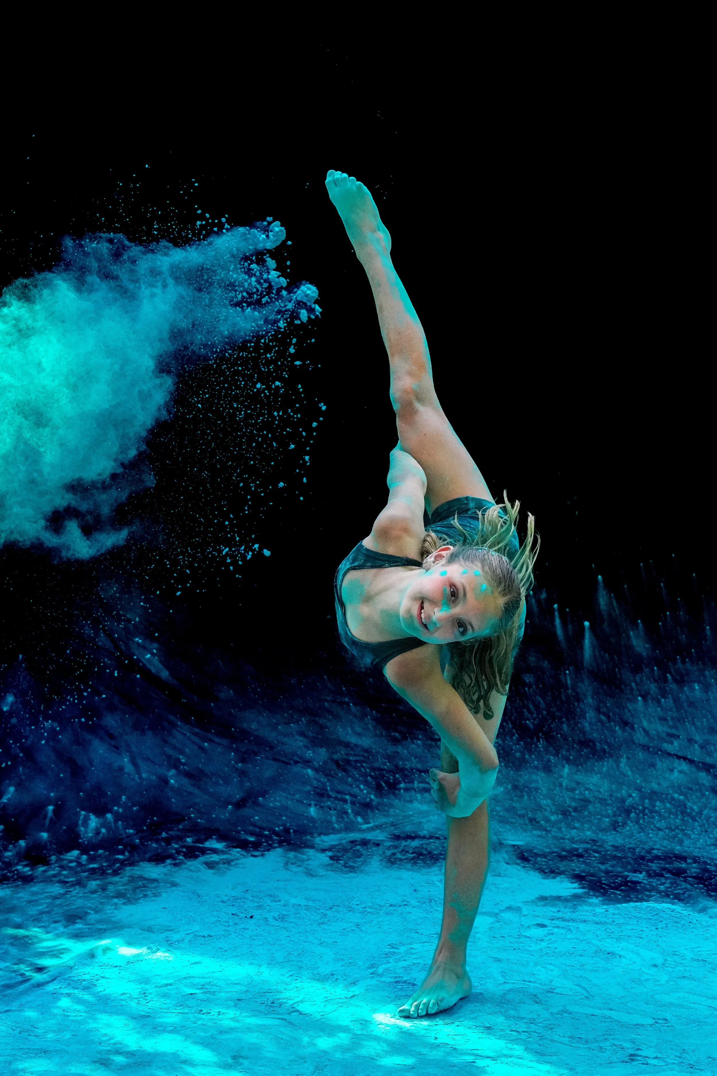 Dance Headquarters student performing a leg extension at studio photoshoot with blue powder.