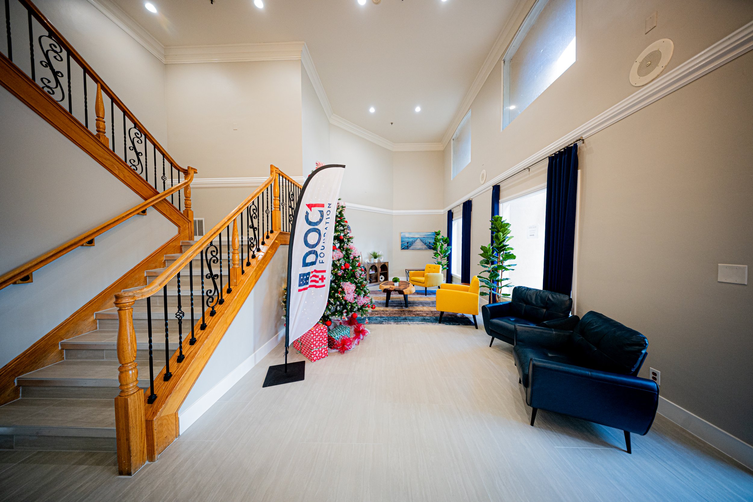 Lobby with staircase, Christmas tree, yellow and black sofas, potted plants, and a banner with American flags.