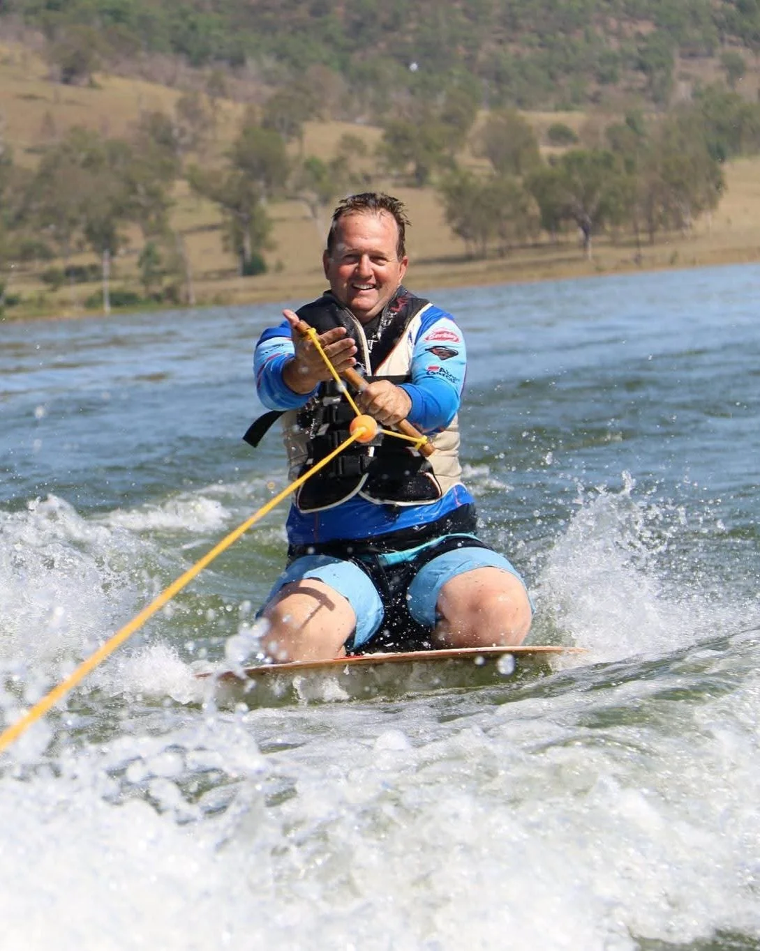 Brad wearing a blue swimsuit and life jacket while being pulled on a disc behind a ski boat.