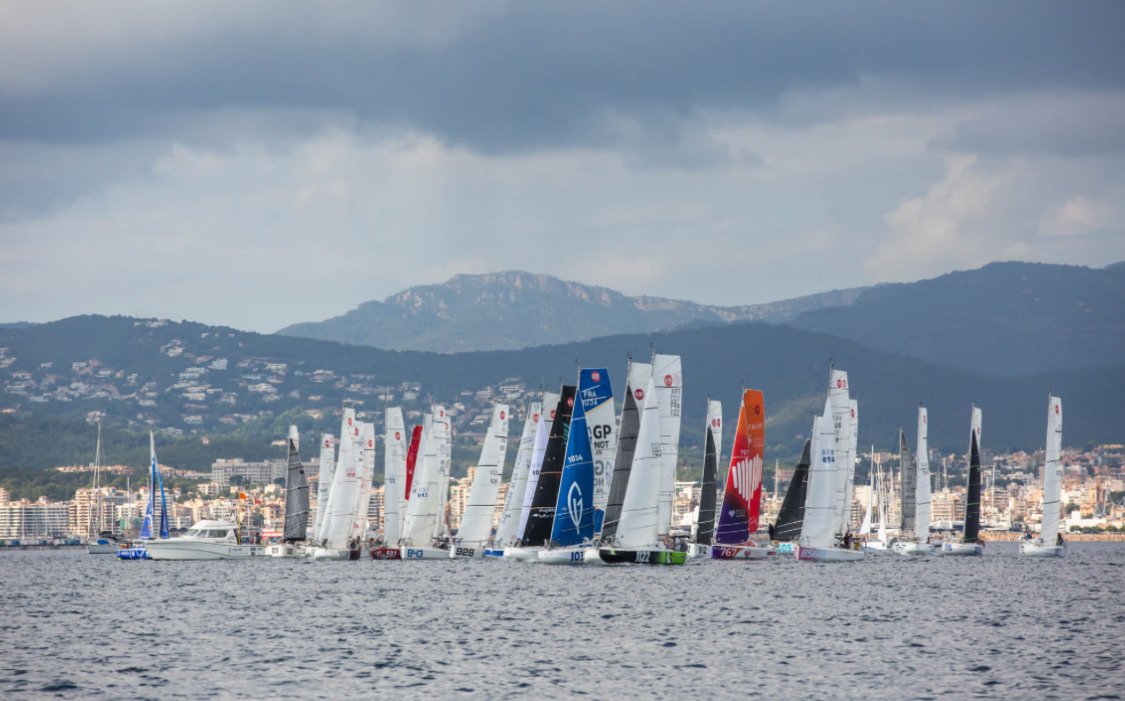 Segelboote beim Rennen vor einer Stadt mit Bergen im Hintergrund.