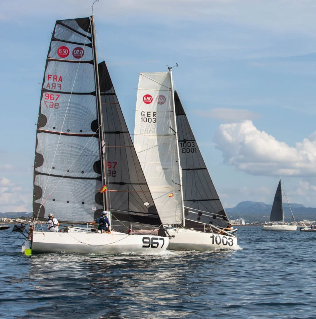 Segelboote auf dem Wasser bei Sonnenschein, mit Bergen im Hintergrund.