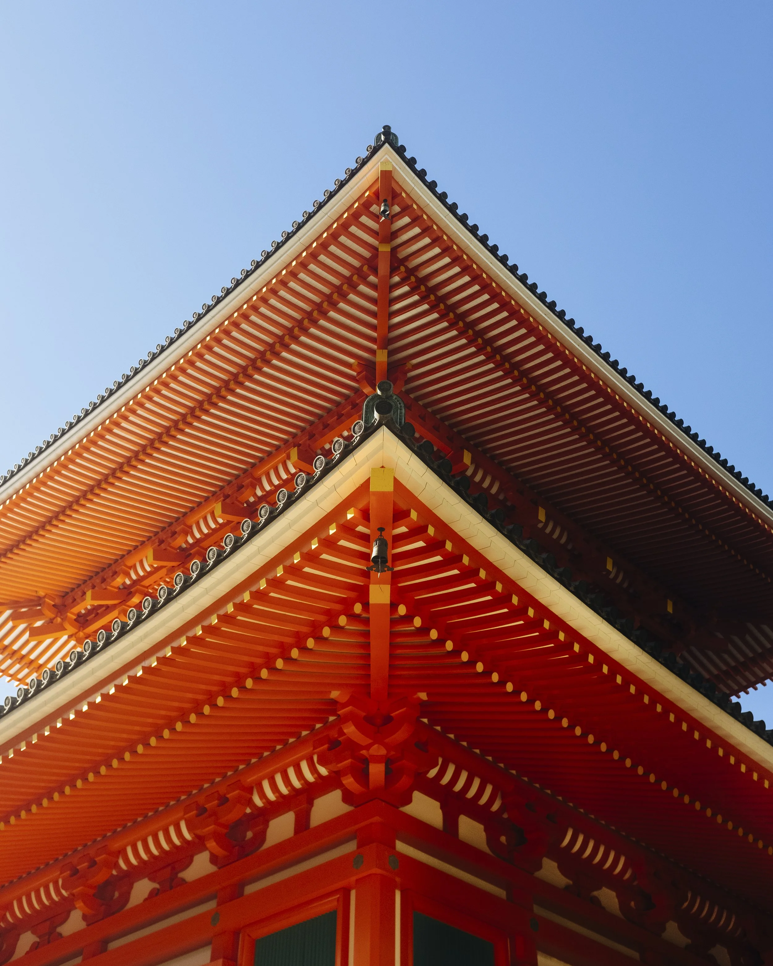 Close-up of a traditional Japanese temple roof with orange and white wooden beams and black decorative tiles against a blue sky.