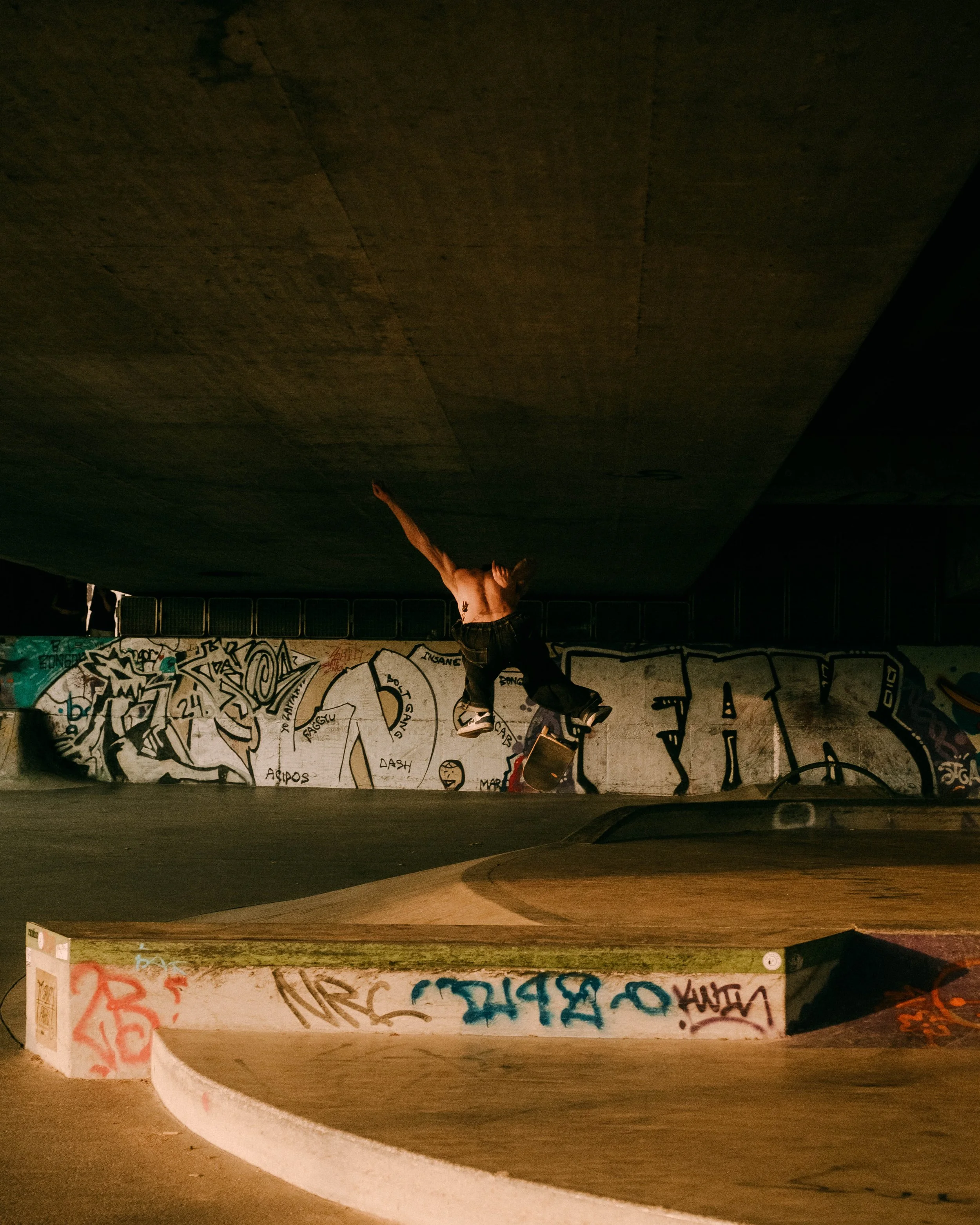Skateboarder performing a trick at night in a graffiti-covered skate park.