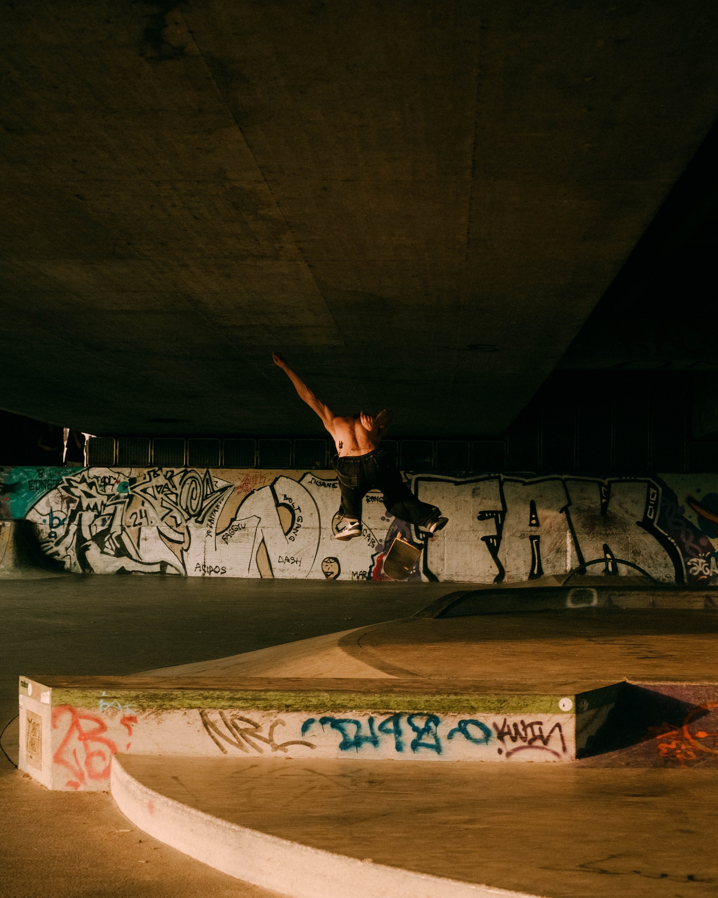 Skateboarder performing a trick at night in a graffiti-covered skate park.