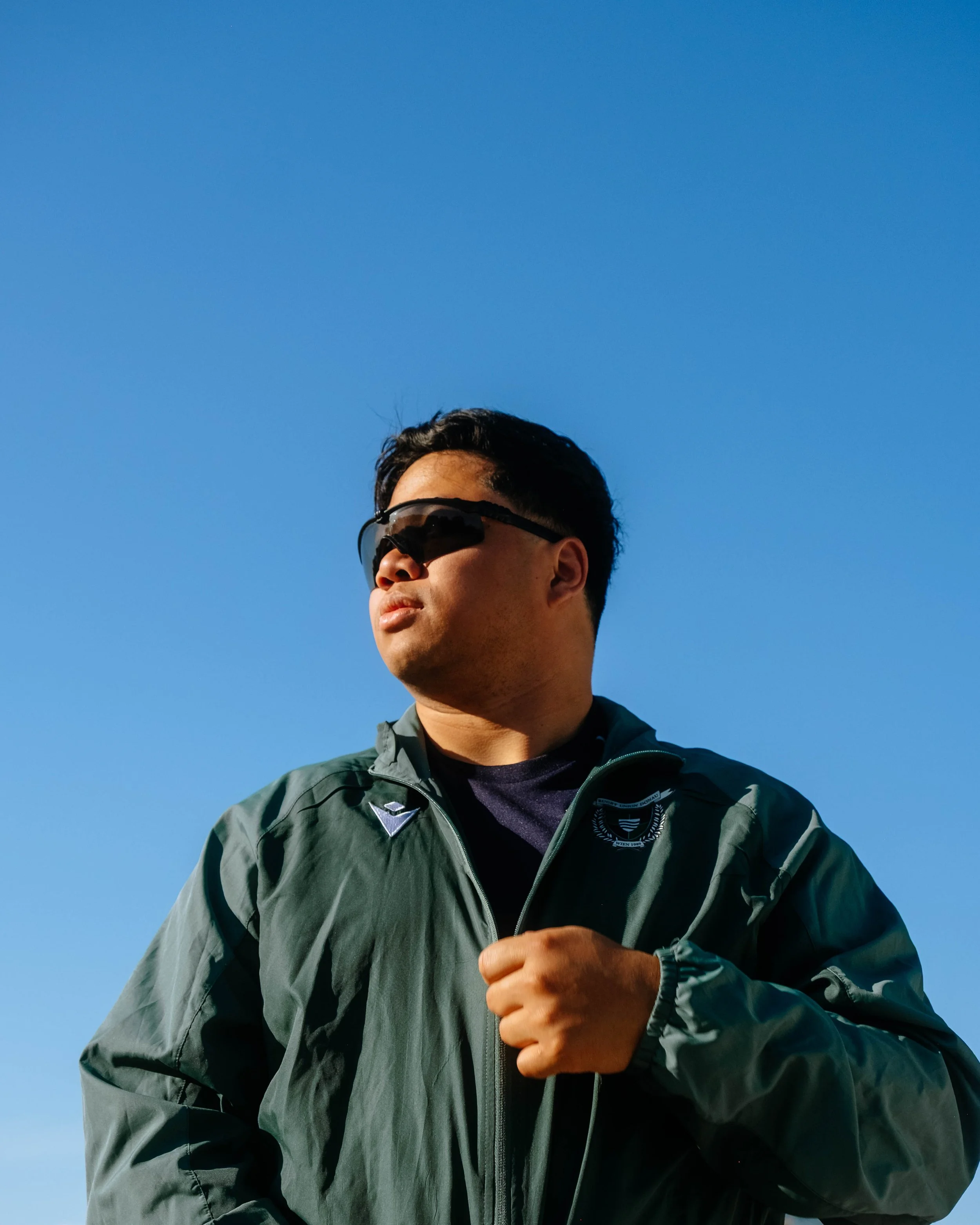 Man wearing sunglasses and a green jacket running outdoors on a clear day.