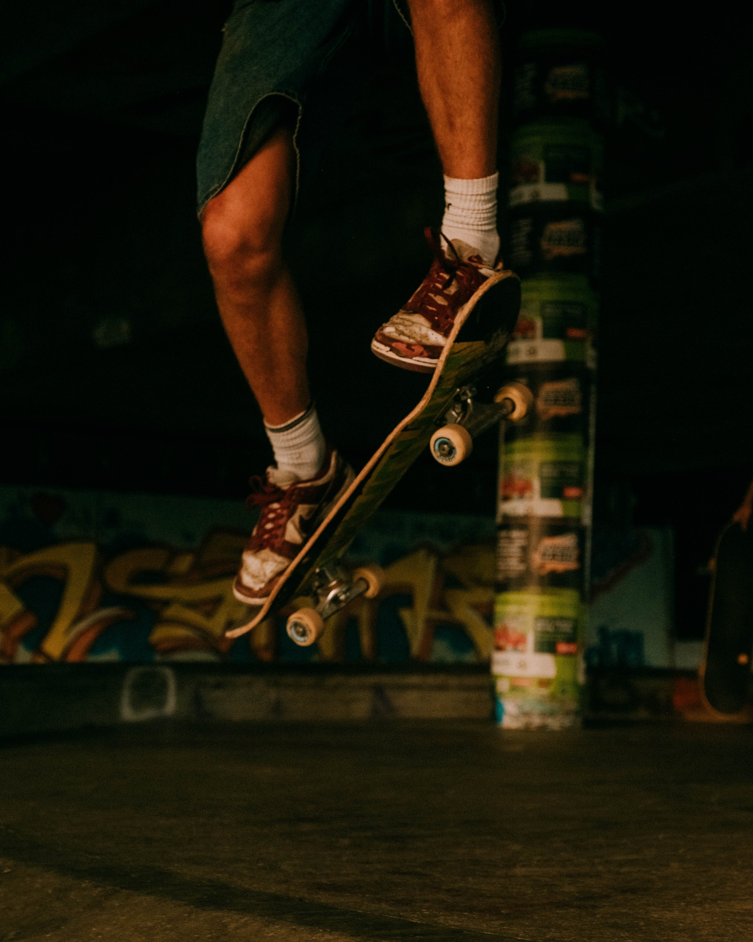 A person skateboarding indoors, wearing white socks, red shoes, and denim shorts, with colorful graffiti in the background.
