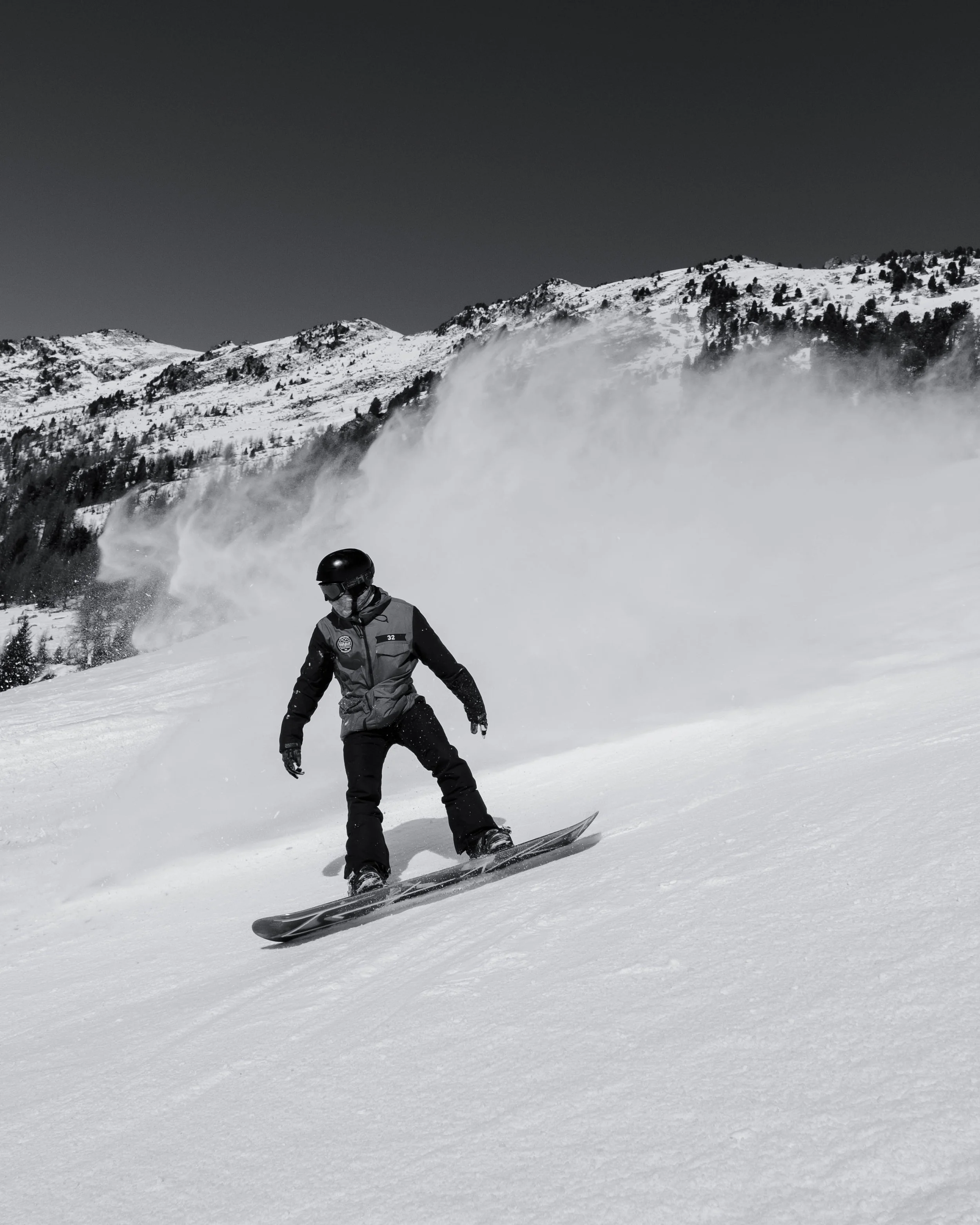 A person snowboarding down a snowy slope with mountains in the background, captured in black and white.