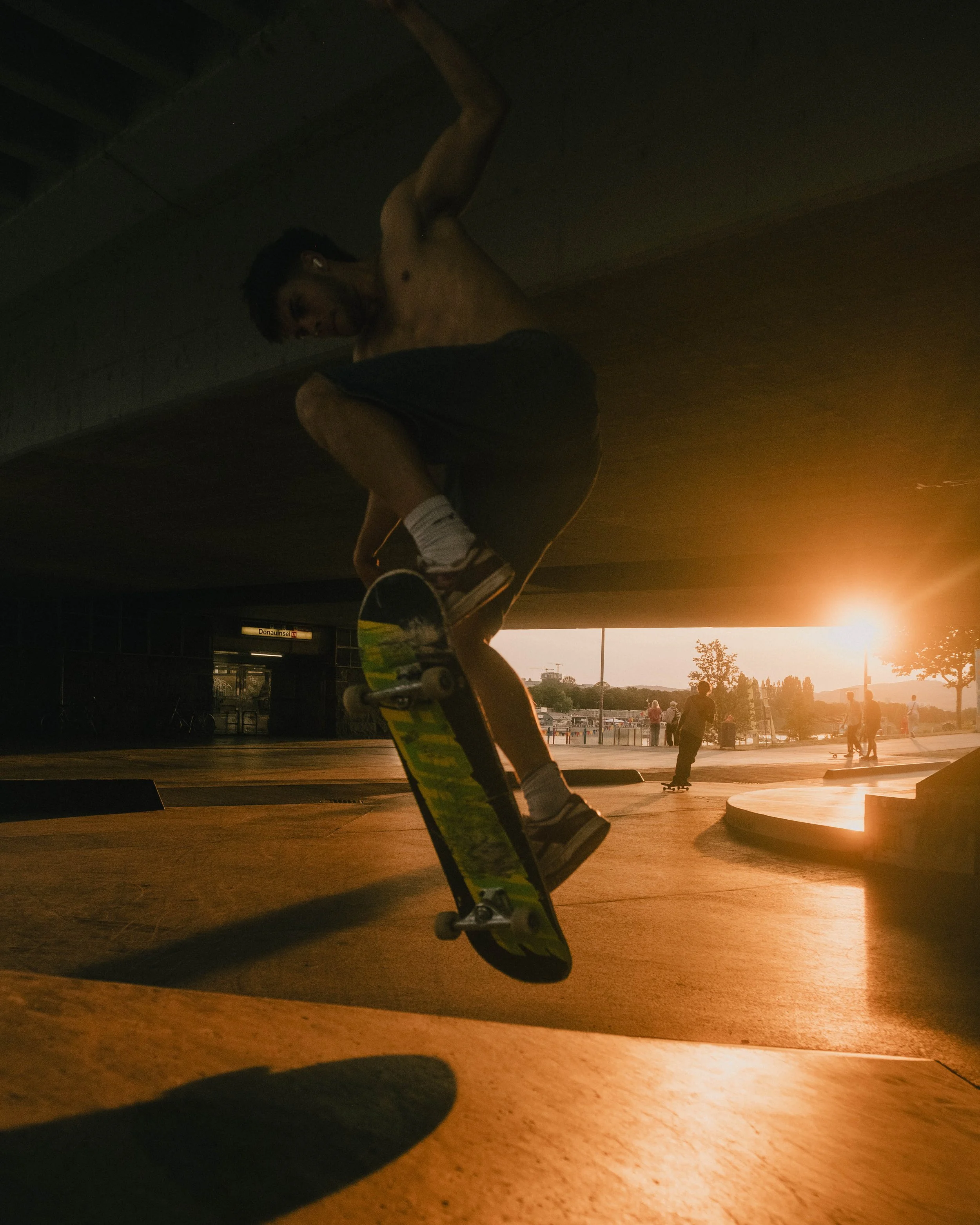 Skateboarder performing a trick under a bridge at sunset.