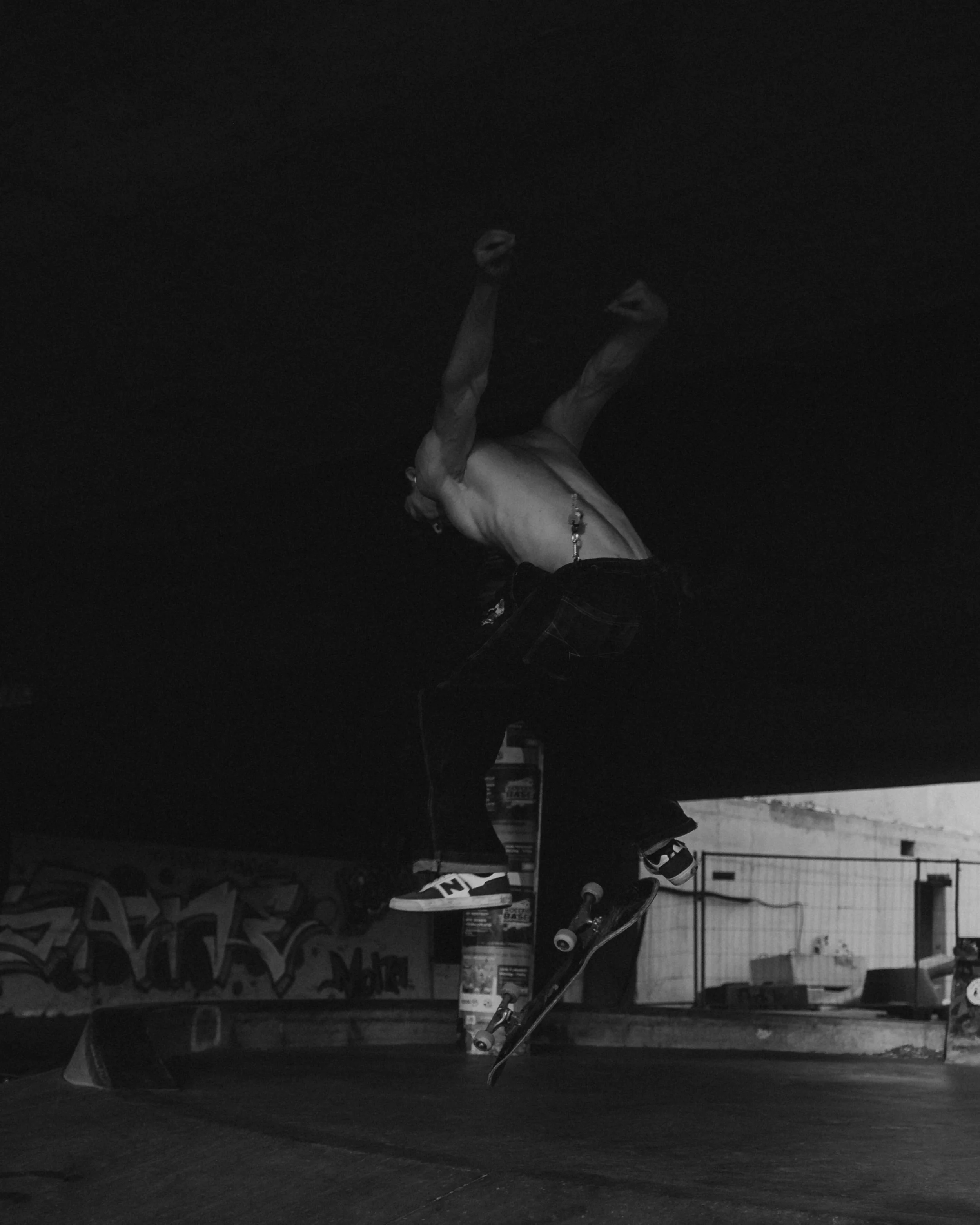 Skateboarder performing a trick at an indoor skate park, with graffiti on the wall in the background, in black and white.