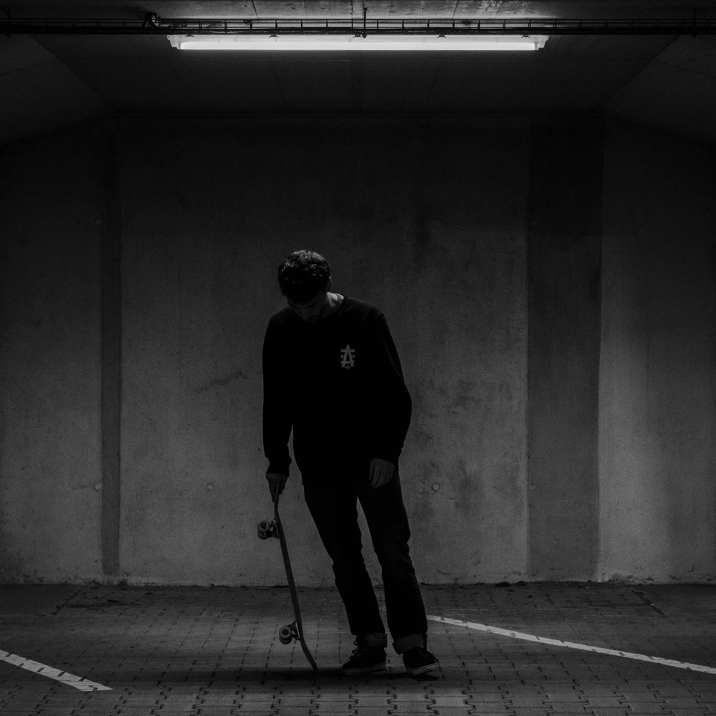 A person with a skateboard standing in a dimly lit, empty parking garage.