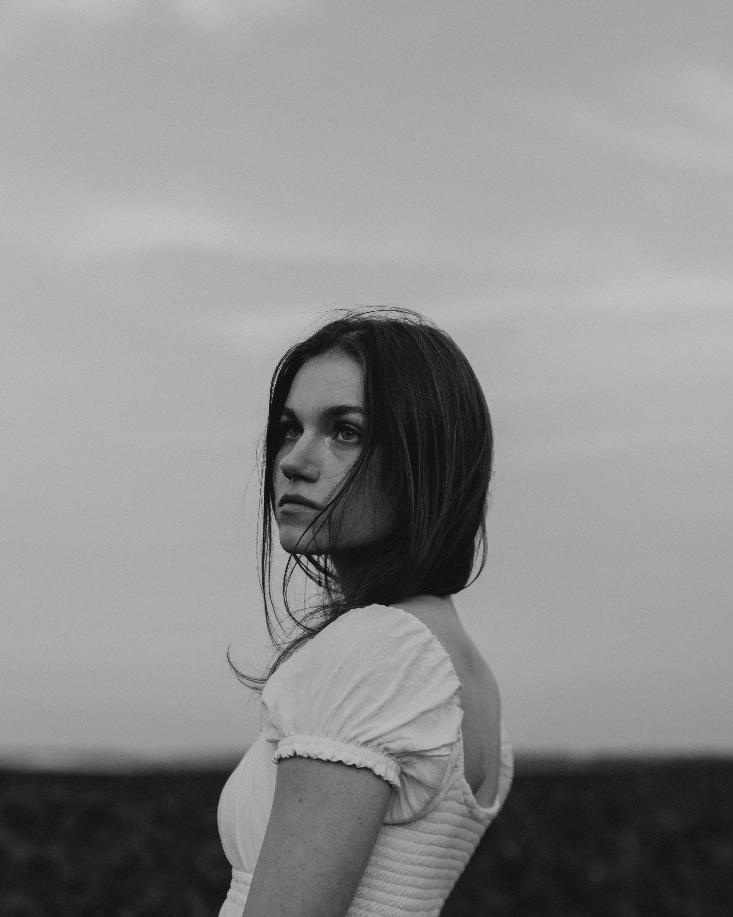 A black and white photo of a woman with shoulder-length dark hair looking over her shoulder outdoors.