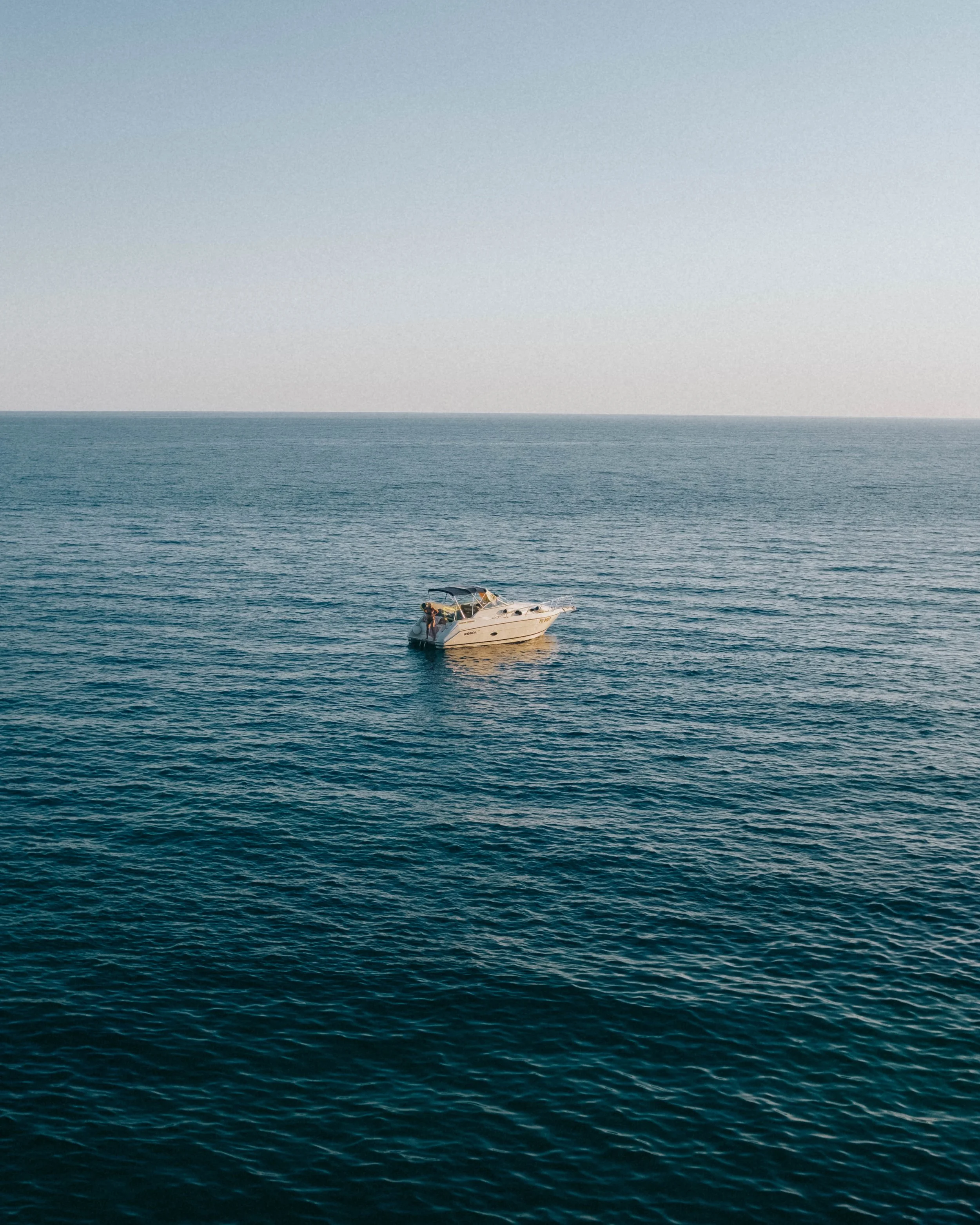 A white yacht floating on calm blue ocean water under a light blue sky.