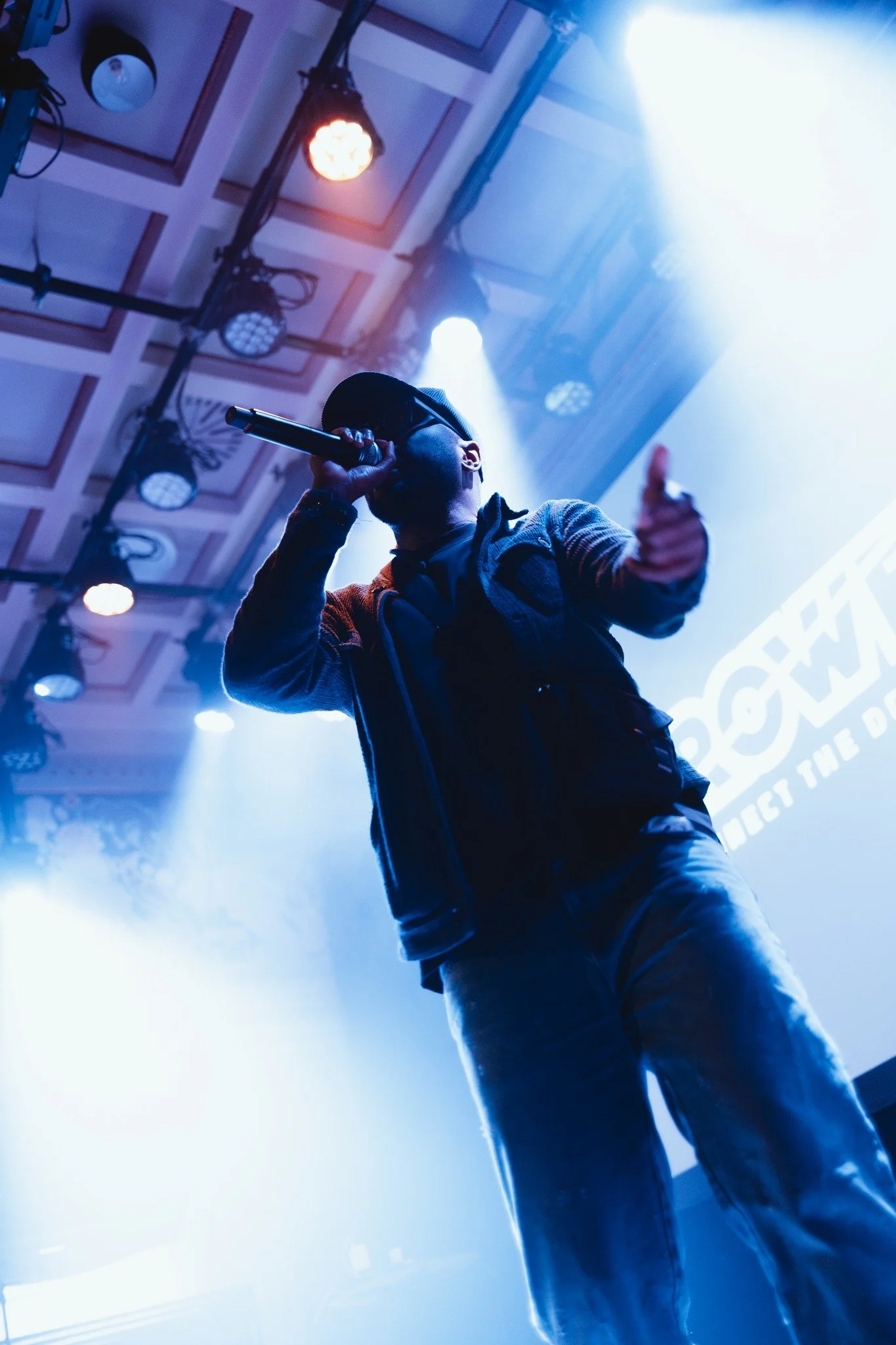 Man performing on stage with microphone in hand under blue lighting in a concert hall.