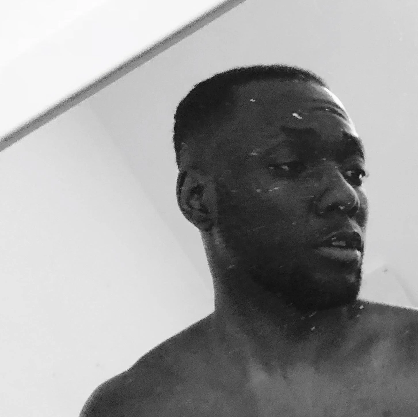 A black and white photo of a shirtless Kendan Adams with low cut/ fade hair, looking with a neutral expression.