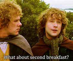 Two young men with curly hair outdoors, engaging in conversation, one replying to a question about second breakfast.