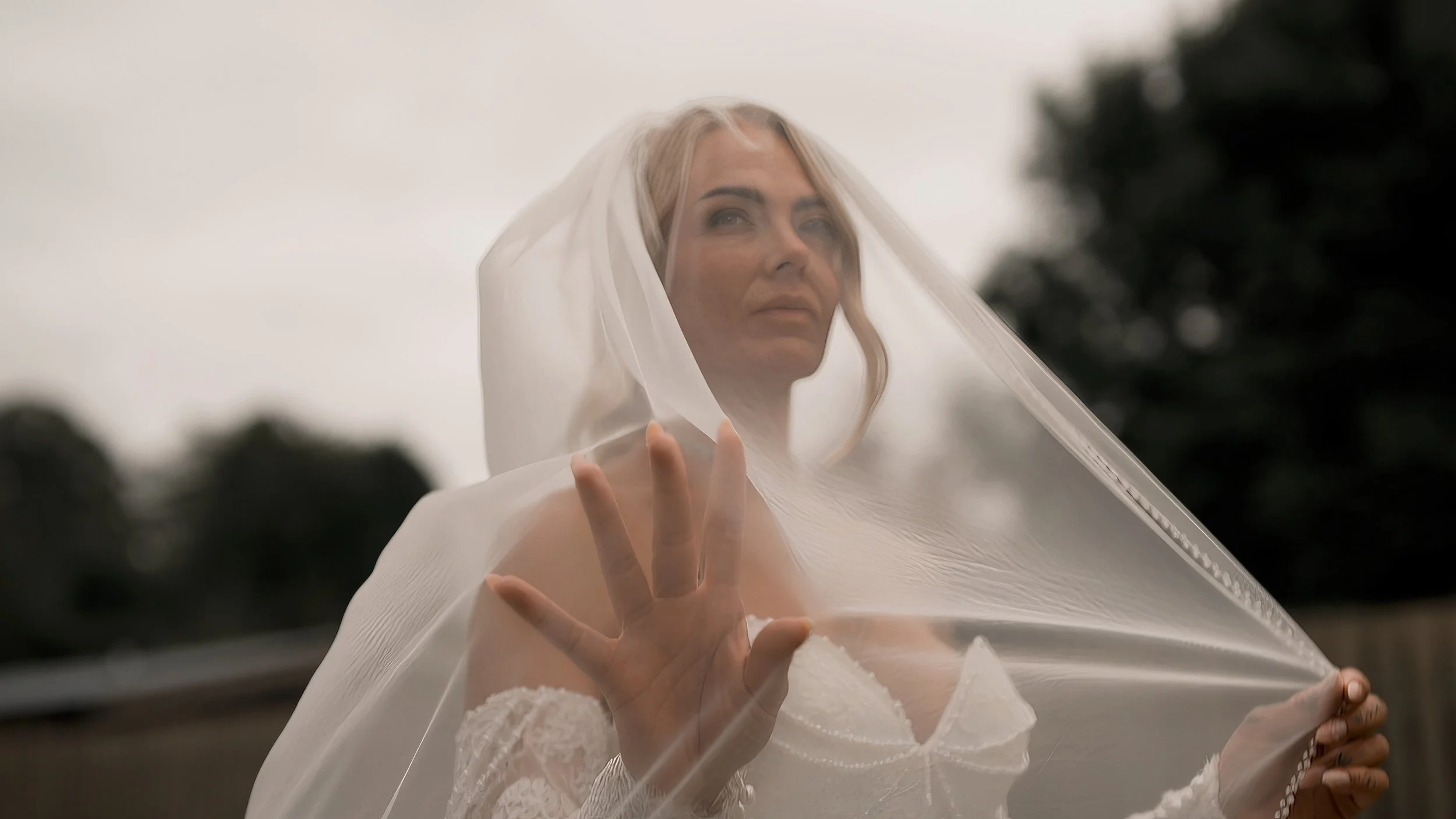 A bride gazing up at the sky, caressing her veil which is draped over her head