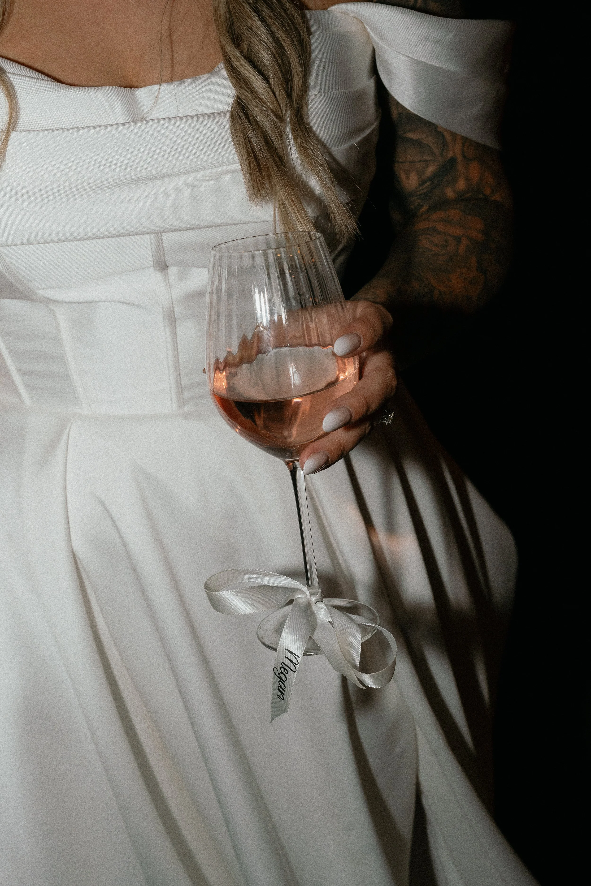 A woman in a white dress holding a glass of rosé wine with a white ribbon tied around the stem.
