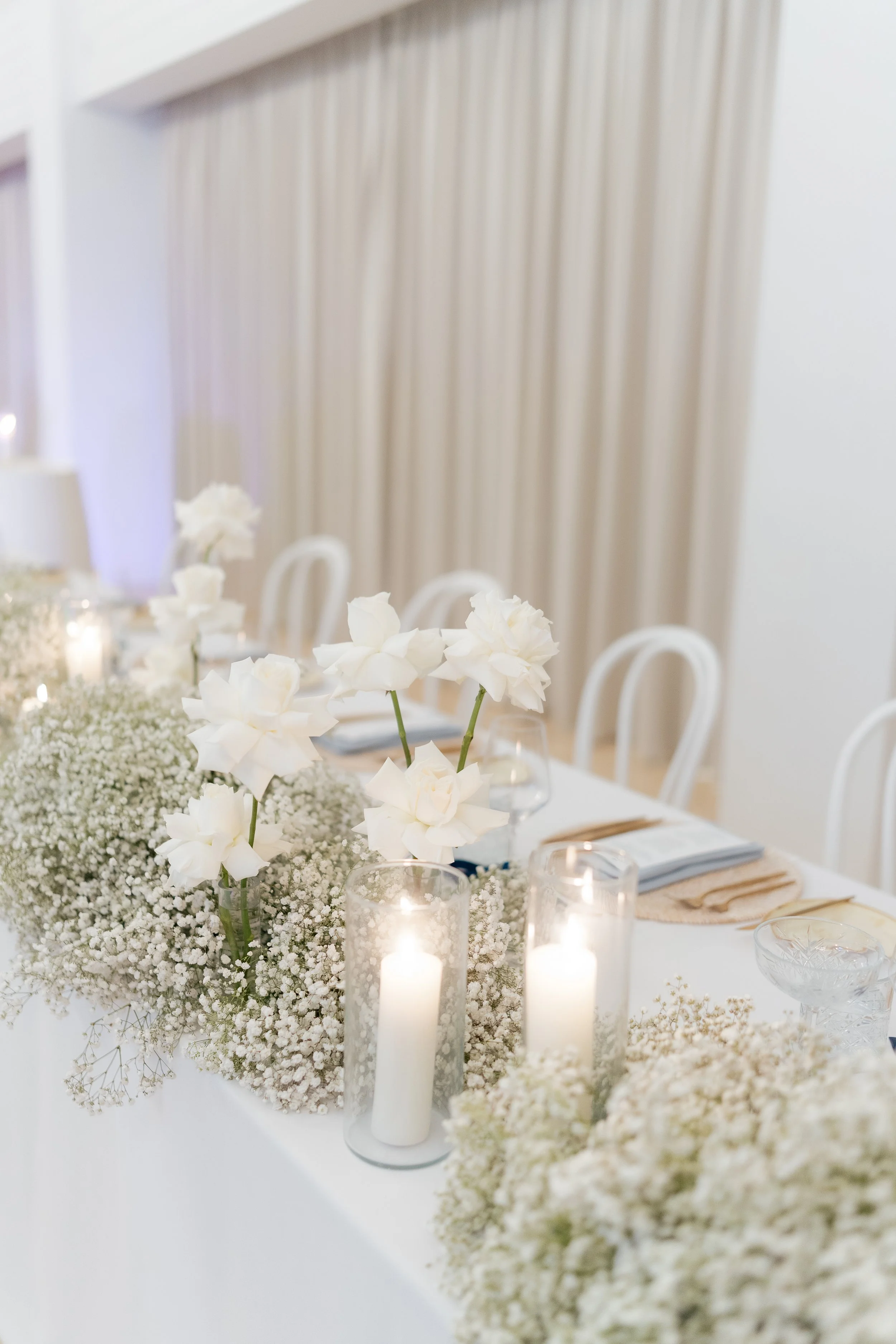Elegant wedding table centerpiece with white flowers and candles on a white tablecloth.