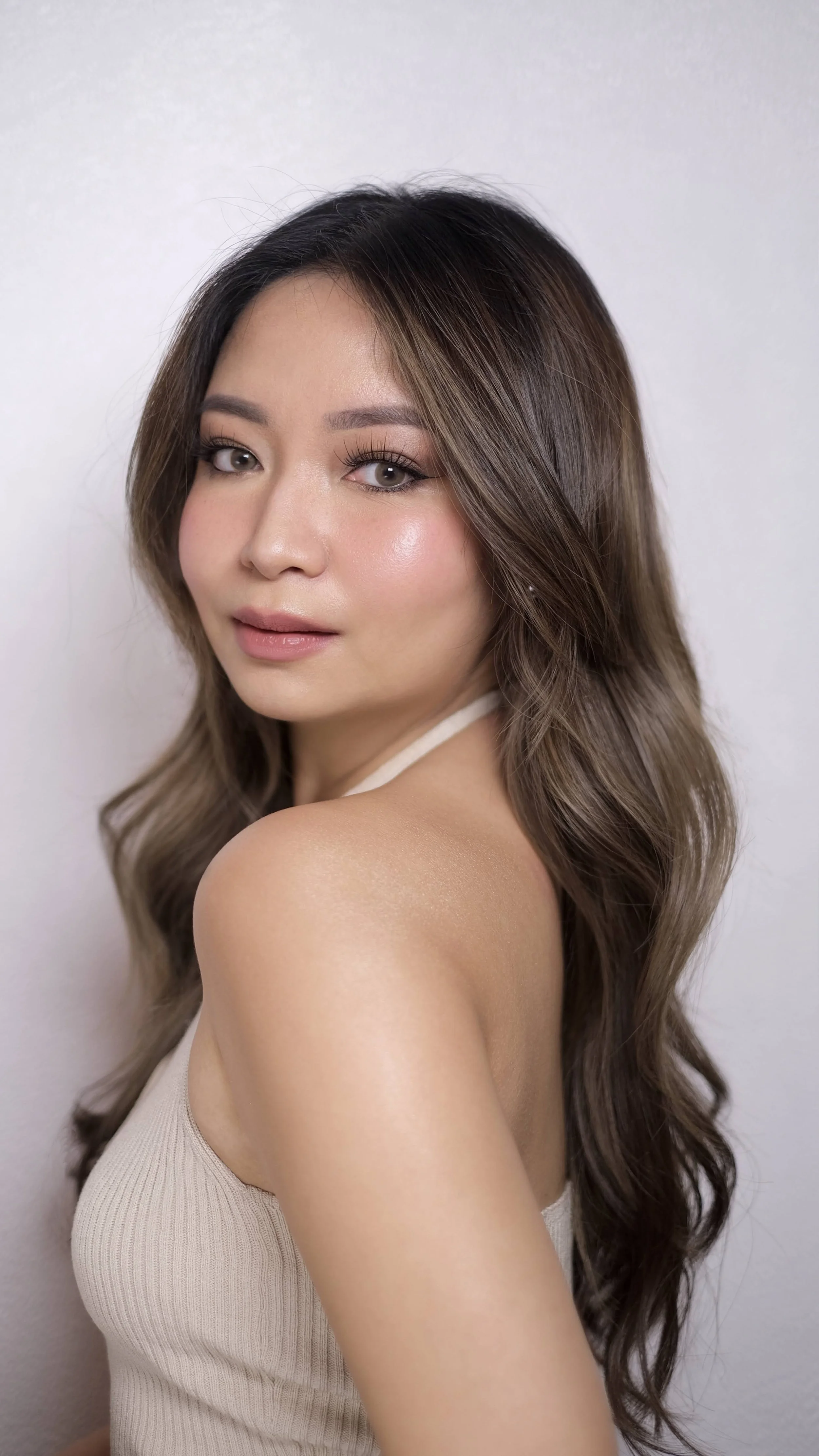 A young woman with wavy brown hair and light skin posing against a plain white wall.