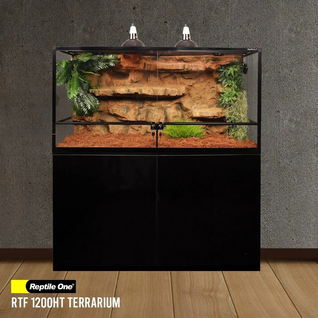 A reptile terrarium with naturalistic rocks, plants, and a substrate base, enclosed in a glass tank on a black stand, against a textured wall and wooden floor.