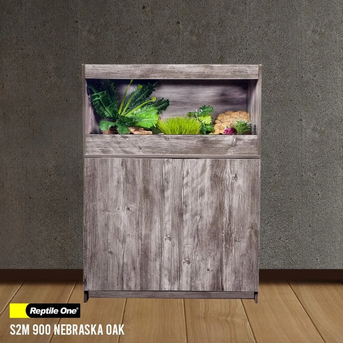 A wooden planter box with various green plants against a textured gray wall and a wooden floor.