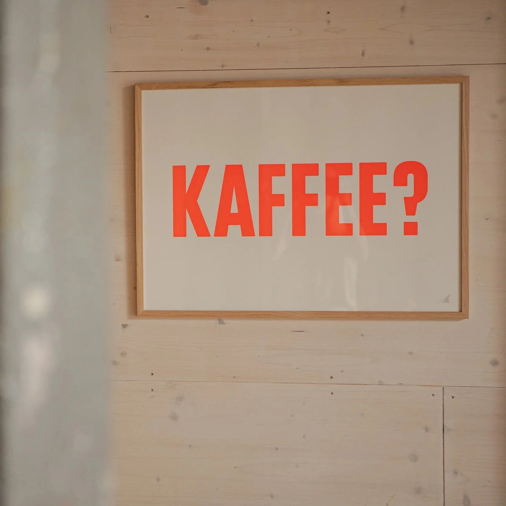 Weißes Schild mit roter Aufschrift 'KAFFEE?' an einer Holz-Wand.