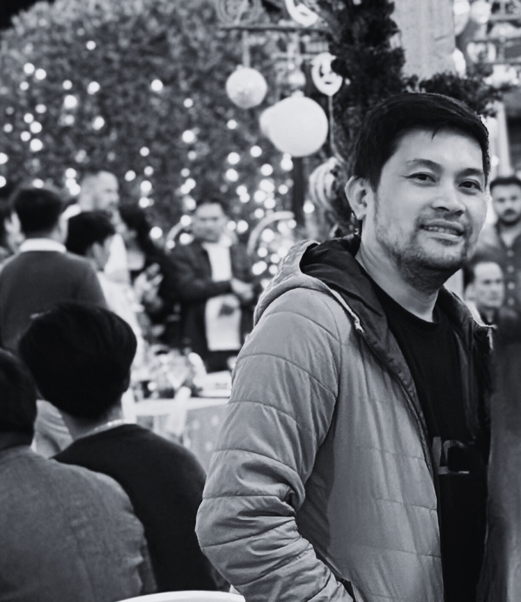 A man smiling at a festive gathering with Christmas decorations and string lights in the background.