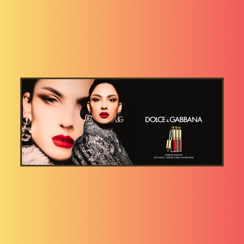 An advertisement for Dolce & Gabbana featuring two women with bold makeup and designer earrings, displaying lip glosses and lipsticks.