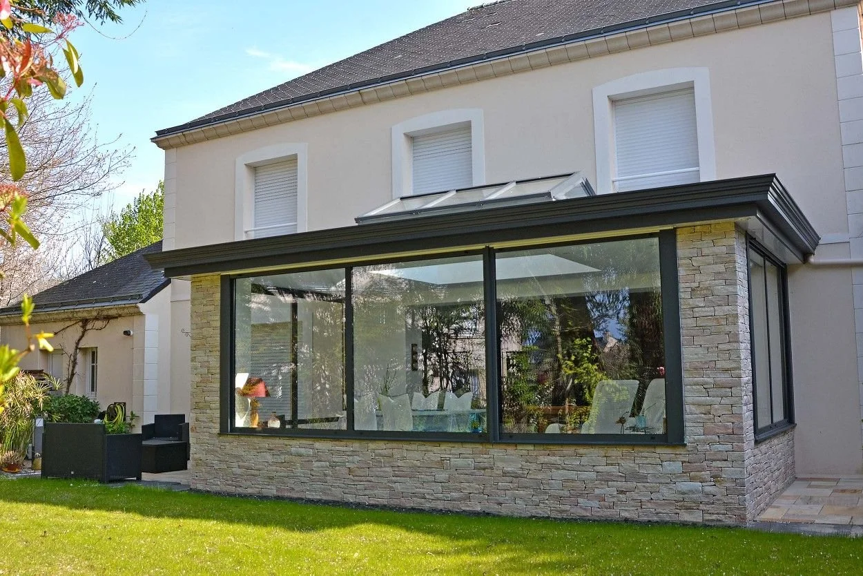 Maison avec extension en verre, murs en pierre, jardin avec mobilier d'extérieur